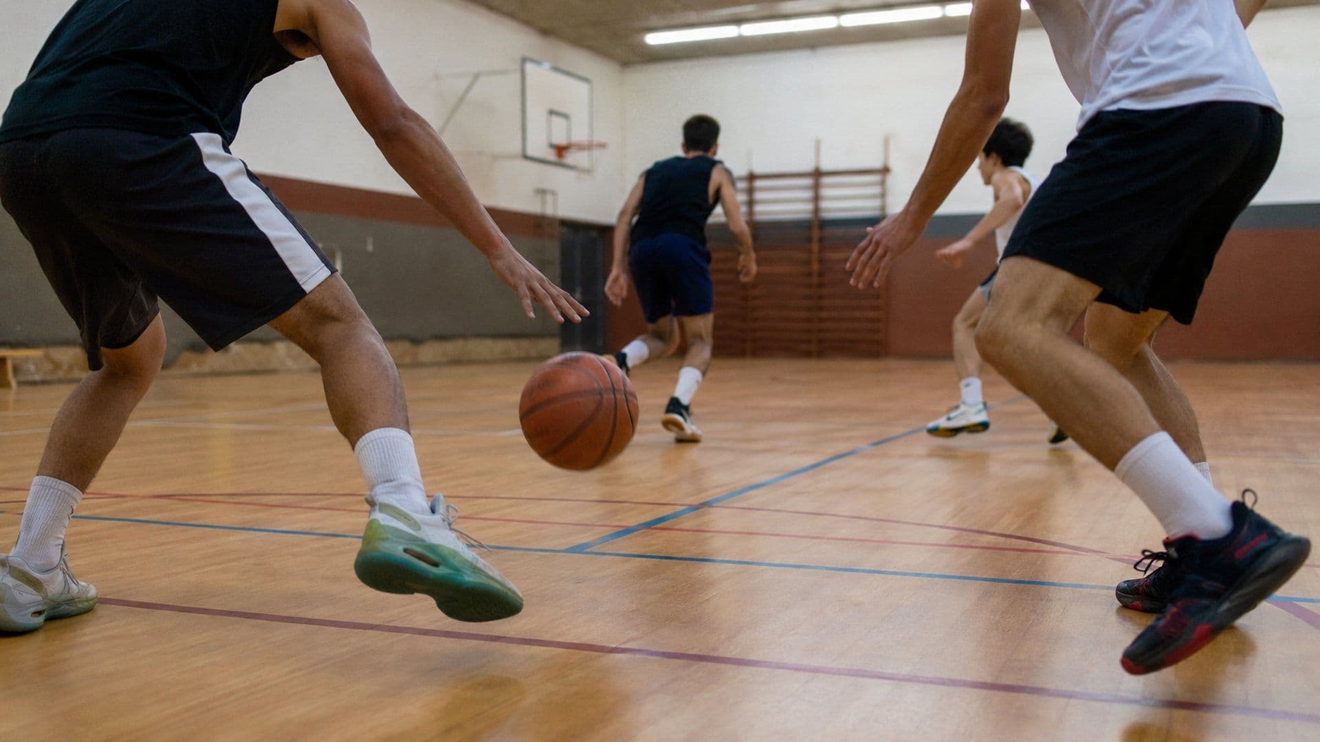 Jogadores em exercício de basquetebol com oposição, bola em movimento num pavilhão